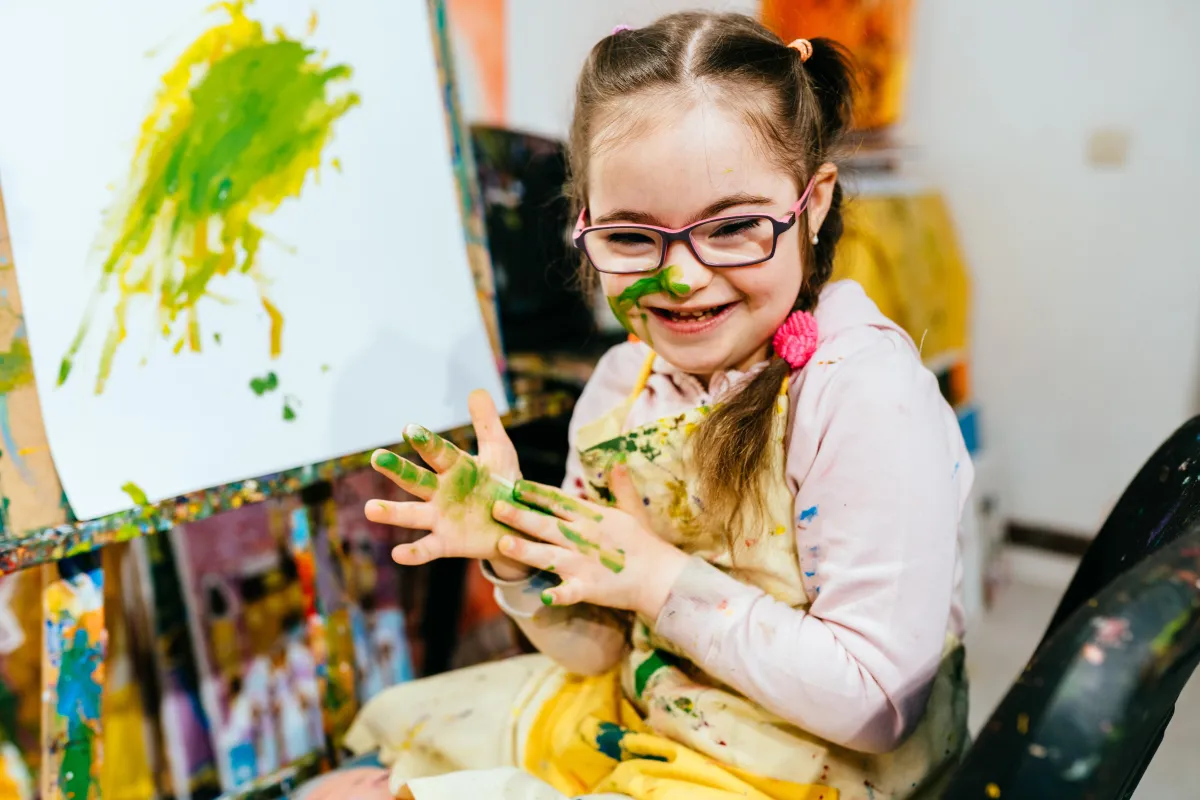 Smiling child engaged in messy painting with green and yellow paint, enjoying sensory play and creative expression