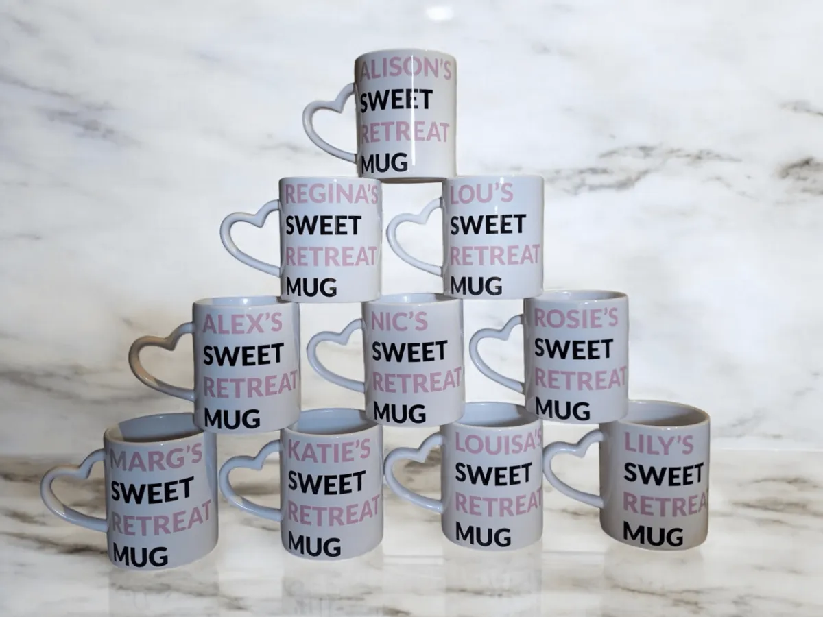 10 white, heart handled mugs stacked in a triangle on a white and grey marble background with the words sweet retreat 