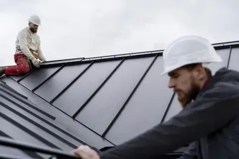 Two roofers in hard hats fitting standing seam metal panels on a commercial building by Brooklyn Park Commercial Roofing