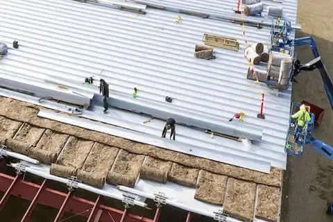 Aerial view of roofing crew installing corrugated metal panels on large commercial building in Brooklyn Park