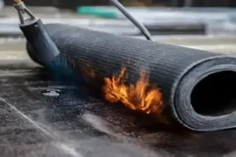 Torch flame applied to modified bitumen roll during flat roof installation in Brooklyn Park