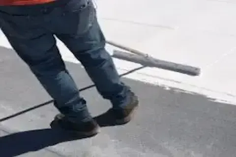 Contractor rolling liquid coating across flat commercial roof surface in Brooklyn Park