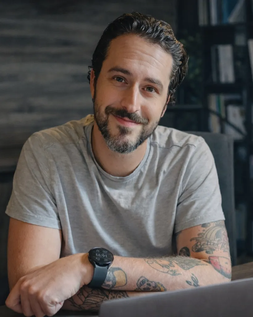 Man smiling at a desk while working on a laptop in an office setting