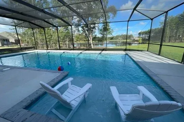 Screened pool enclosure with bronze aluminum frame overlooking a pond, with lounge chairs and pool floats, at a Hammock Bay home in Freeport, FL