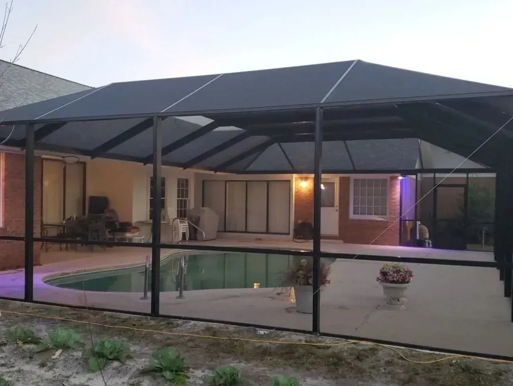 Bronze mansard pool enclosure over a lit pool and covered patio at dusk, built by Aluminum Building Systems in Mary Esther, FL