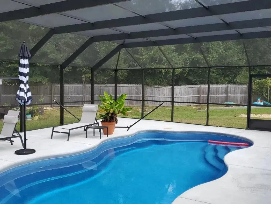 Bronze mansard pool screen enclosure over a freeform pool with lounge chairs, installed by Aluminum Building Systems in Navarre, FL