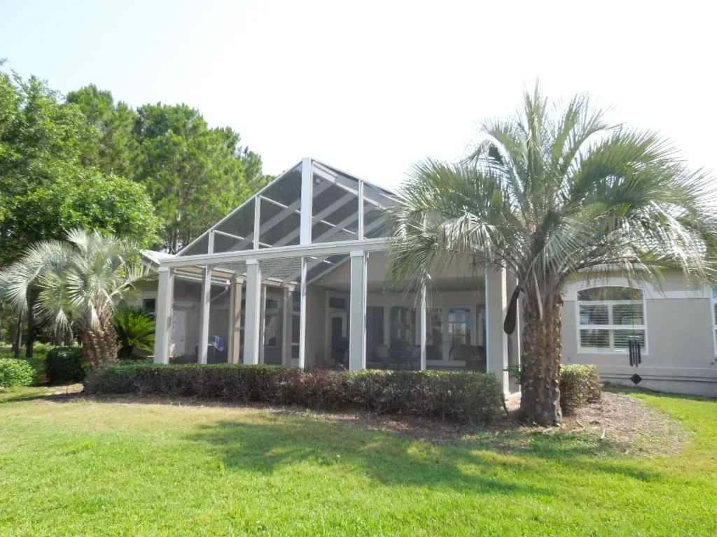 White aluminum gable screen enclosure over a covered lanai beside a palm tree, built by Aluminum Building Systems in Miramar Beach, FL