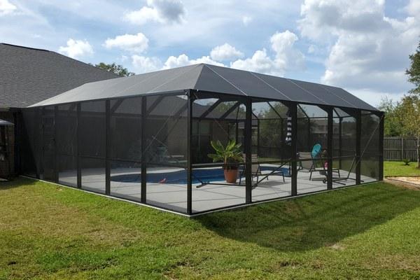 Screened pool enclosure with a hip roof around a backyard pool, built by Aluminum Building Systems
