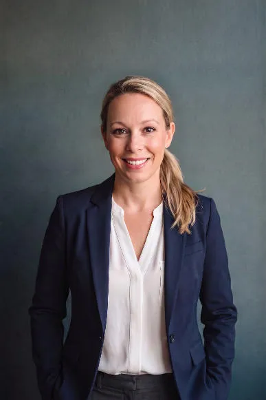 The Cosmic Empress stands in front of a gradient grey backdrop wearing a blue blazer and white button down shirt.