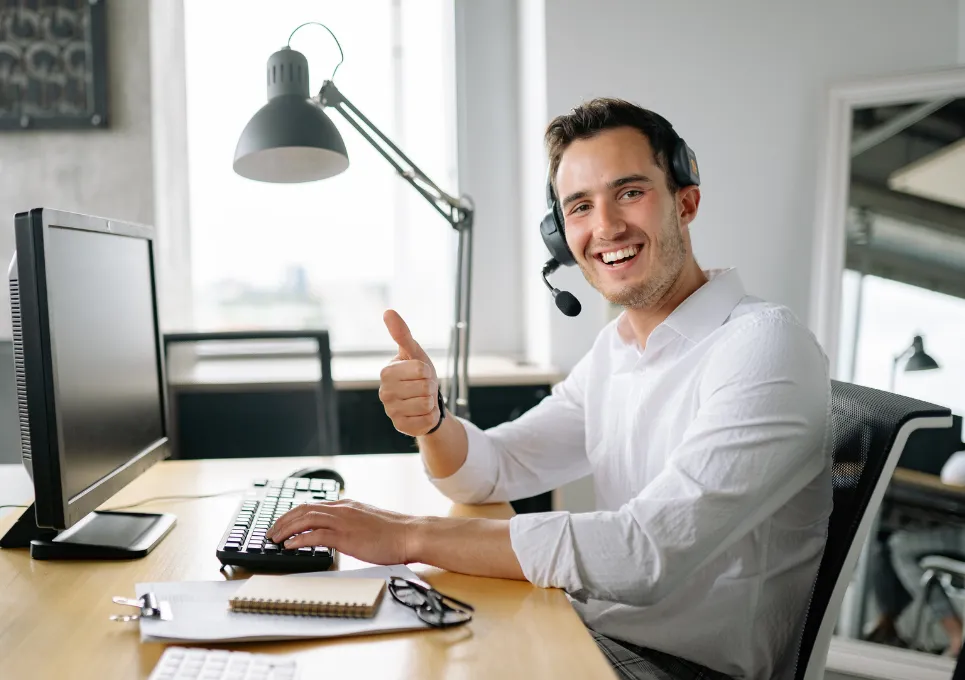 Man sat at a desk with a computer looking very happy