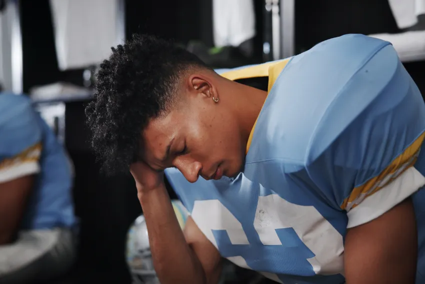 A football player sitting with head down, showing signs of discomfort or possible concussion.
