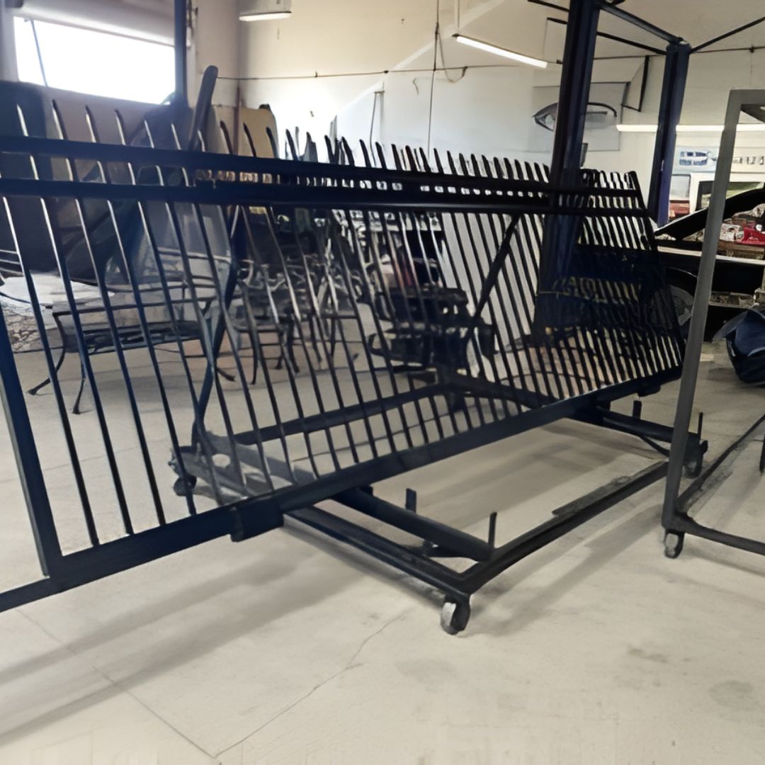 Large sections of black decorative metal fencing are leaning against a rolling metal rack inside a shop.