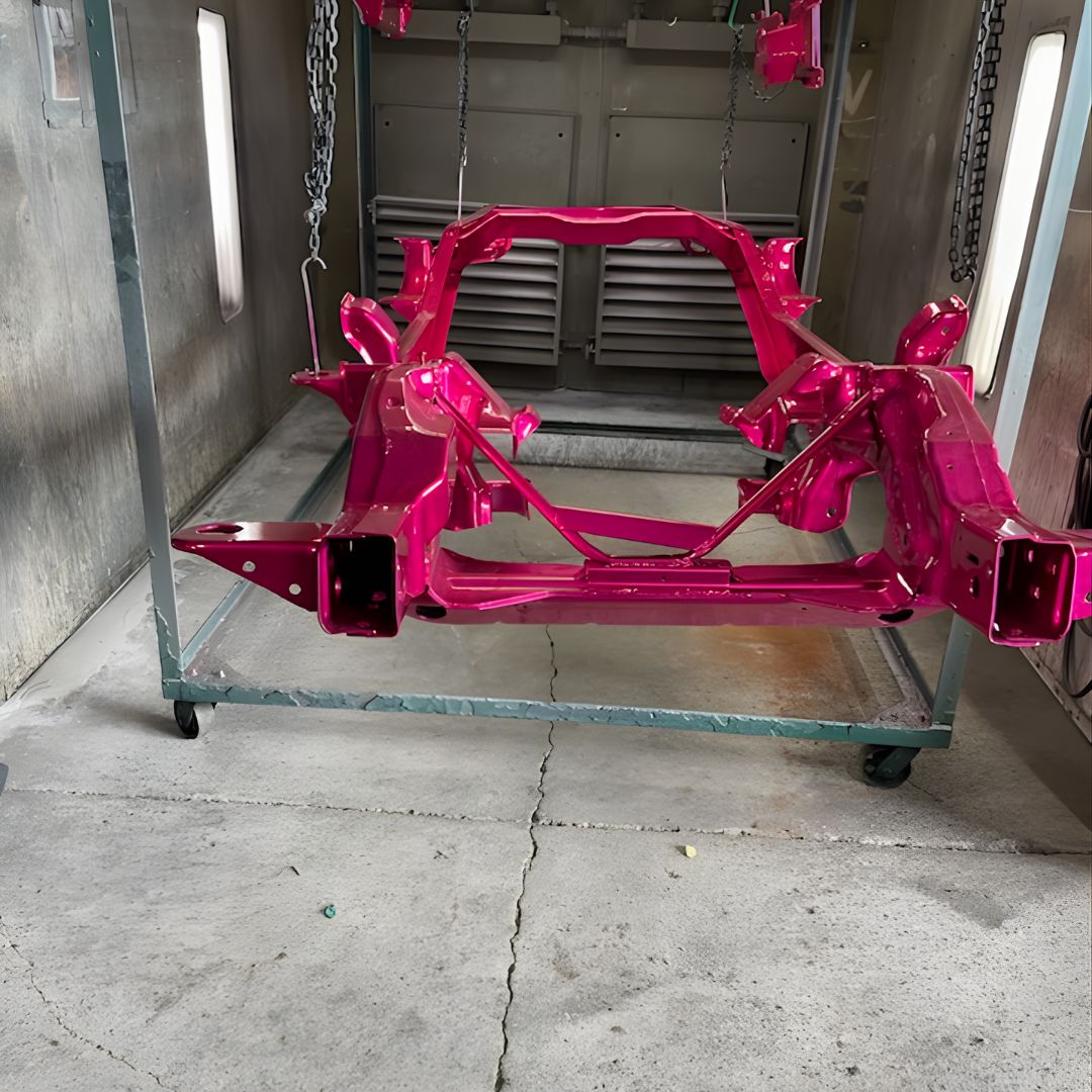 A bare vehicle chassis (frame) that has been freshly painted a bright, glossy hot pink, resting on a rolling rack inside a workshop.