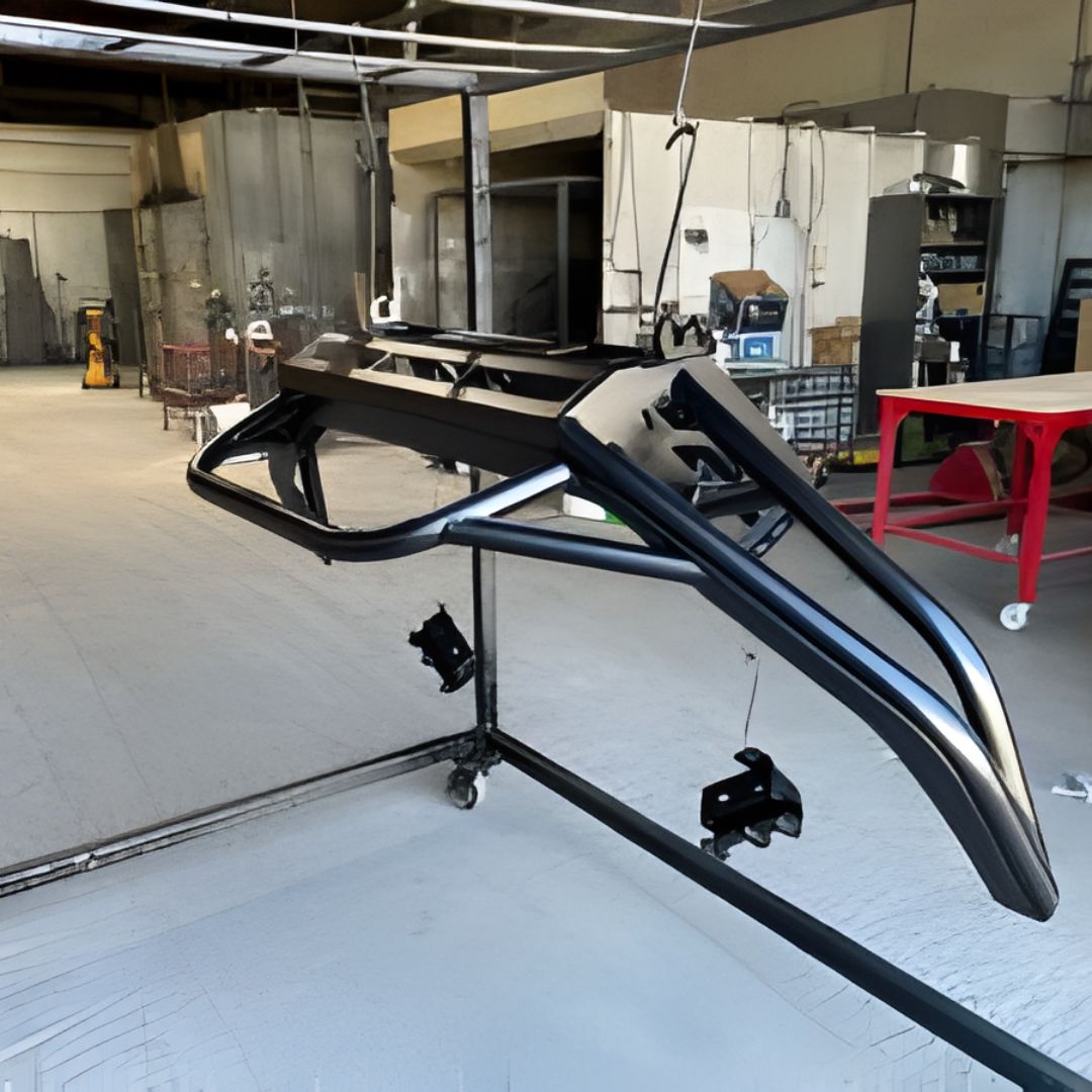 A heavy-duty, tubular black metal bumper (or roll bar) hanging from a rack inside a workshop, likely just painted or powder-coated.