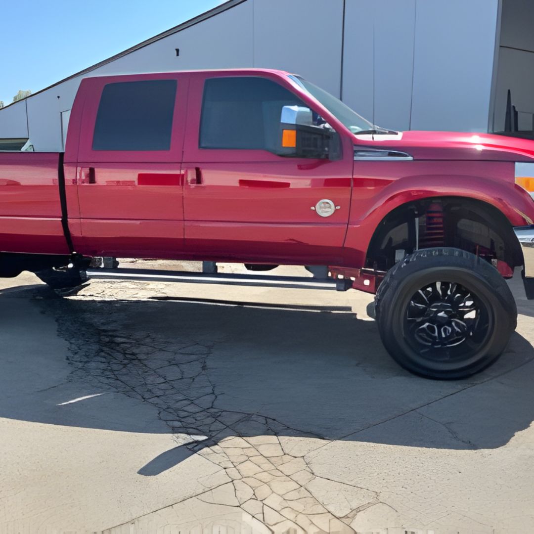 A side-profile view of a lifted, late-model red crew-cab pickup truck parked outdoors on concrete.