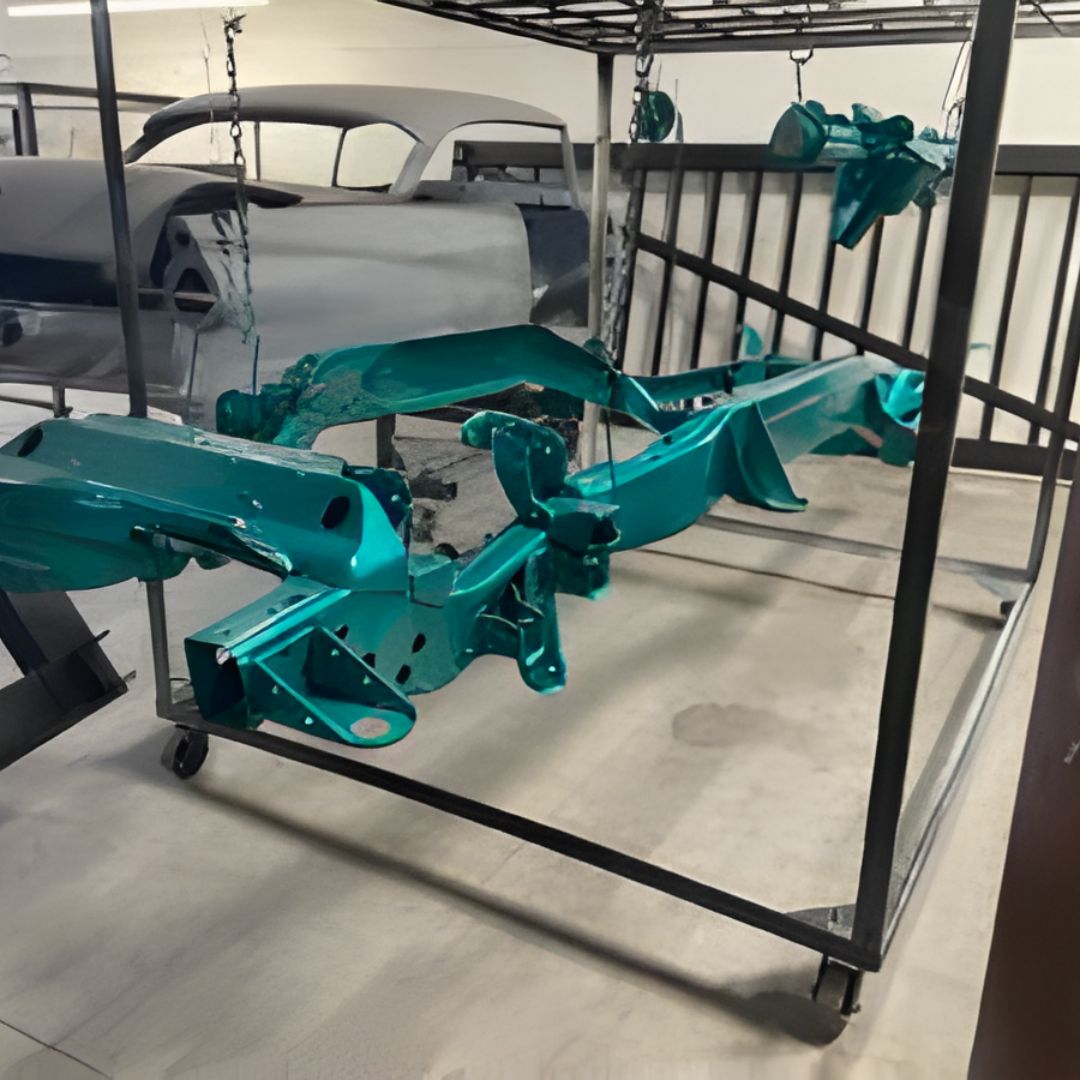 A bare vehicle chassis painted a vibrant teal or turquoise color, resting on a rolling cart in a shop, with a gray car body visible in the background.