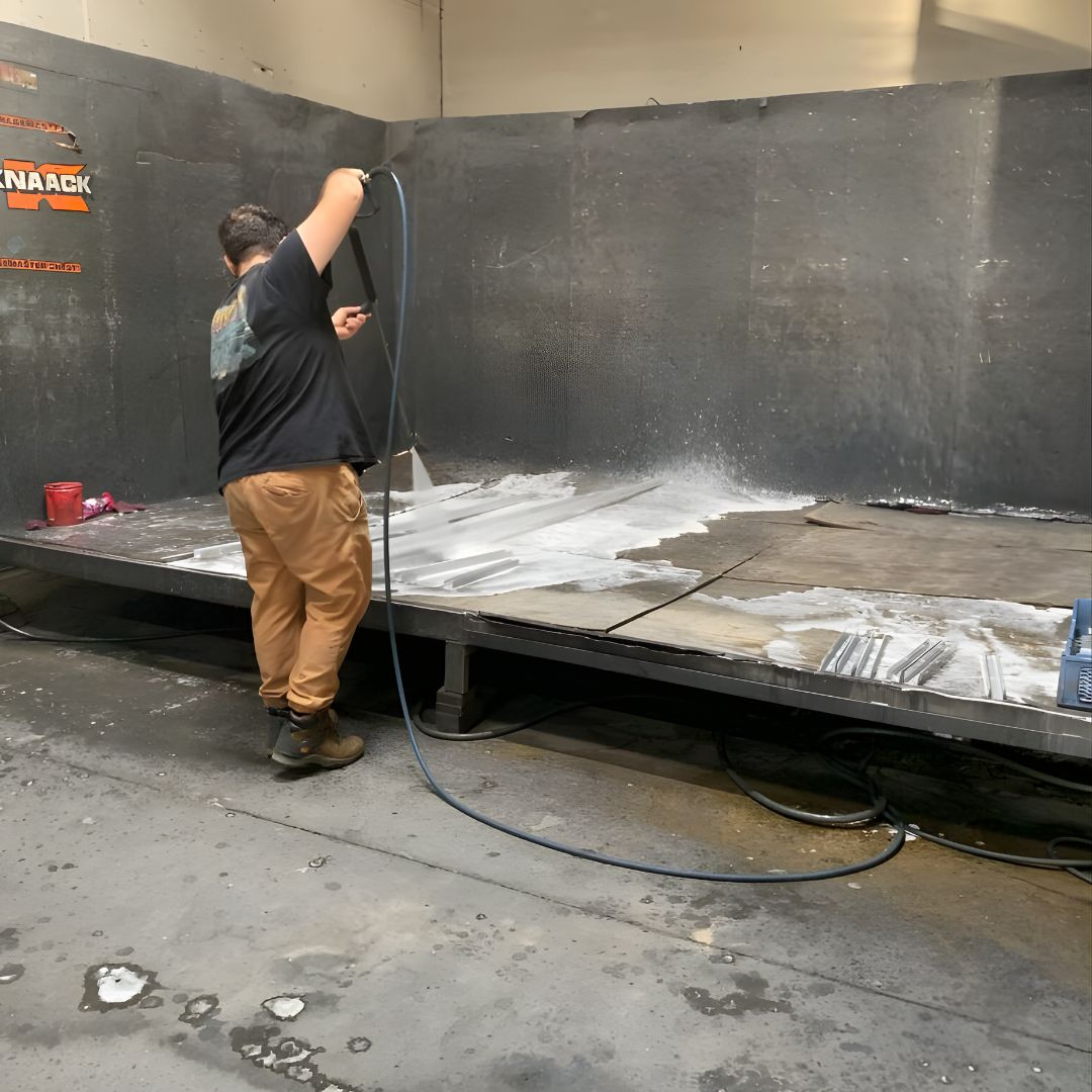 Technician spray cleaning or rinsing metal panels inside a preparation booth before coating.