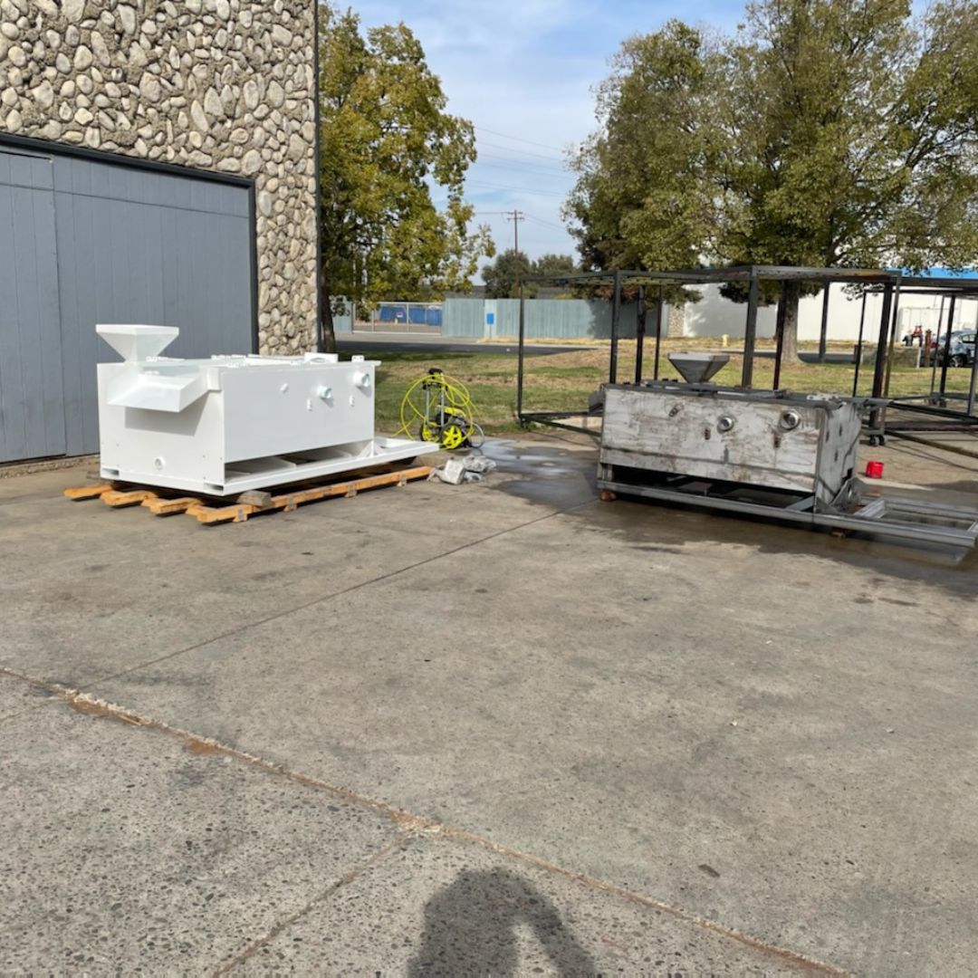 Industrial metal equipment placed on wooden pallets outside a workshop building on a concrete lot.