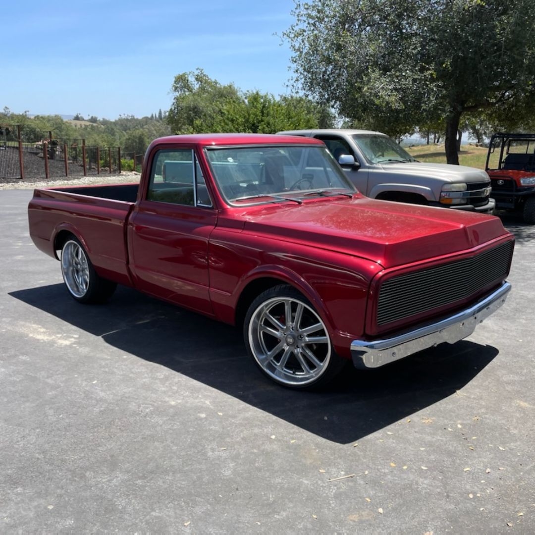 A classic, dark red pickup truck parked outdoors on asphalt, featuring large custom chrome wheels.