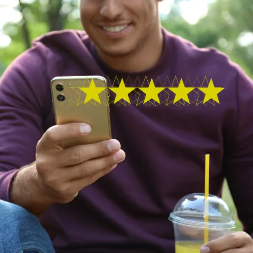 Man smiling while holding a smartphone displaying five yellow stars, symbolizing positive reviews, with a drink beside him in a park setting, highlighting the importance of customer feedback for business reputation and SEO.