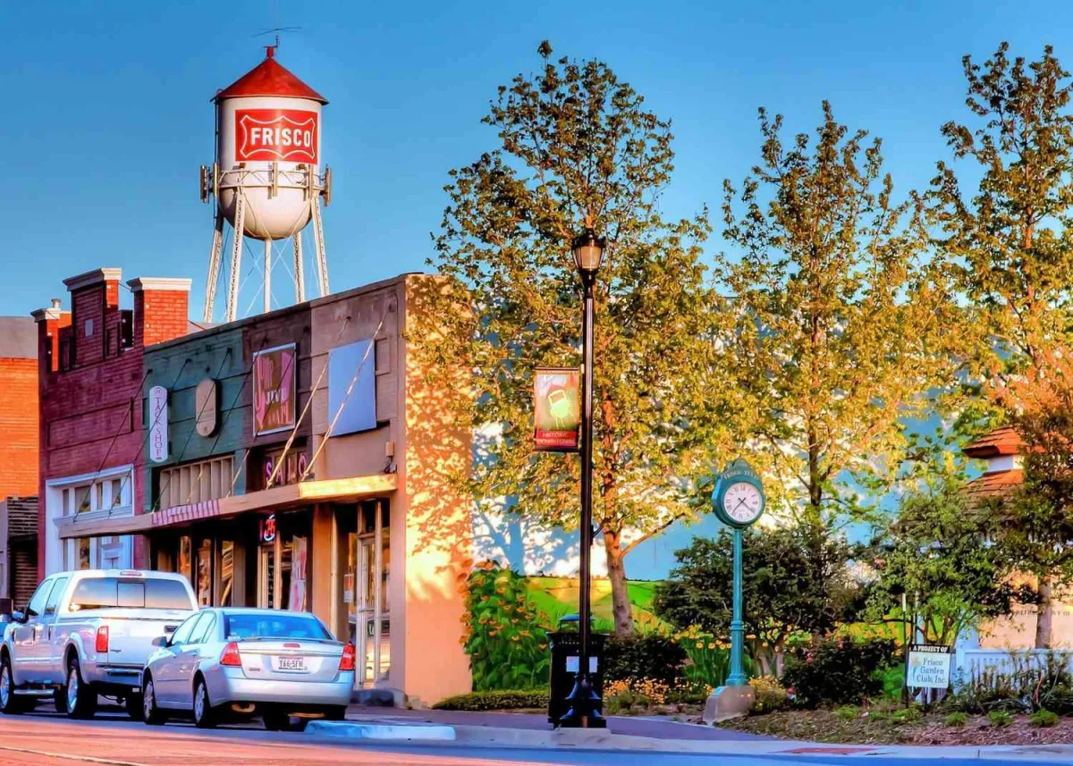 Frisco water tower with "FRISCO" signage, historic buildings, and trees in a vibrant downtown setting, representing OttoMate 360's local commitment to North Texas businesses.