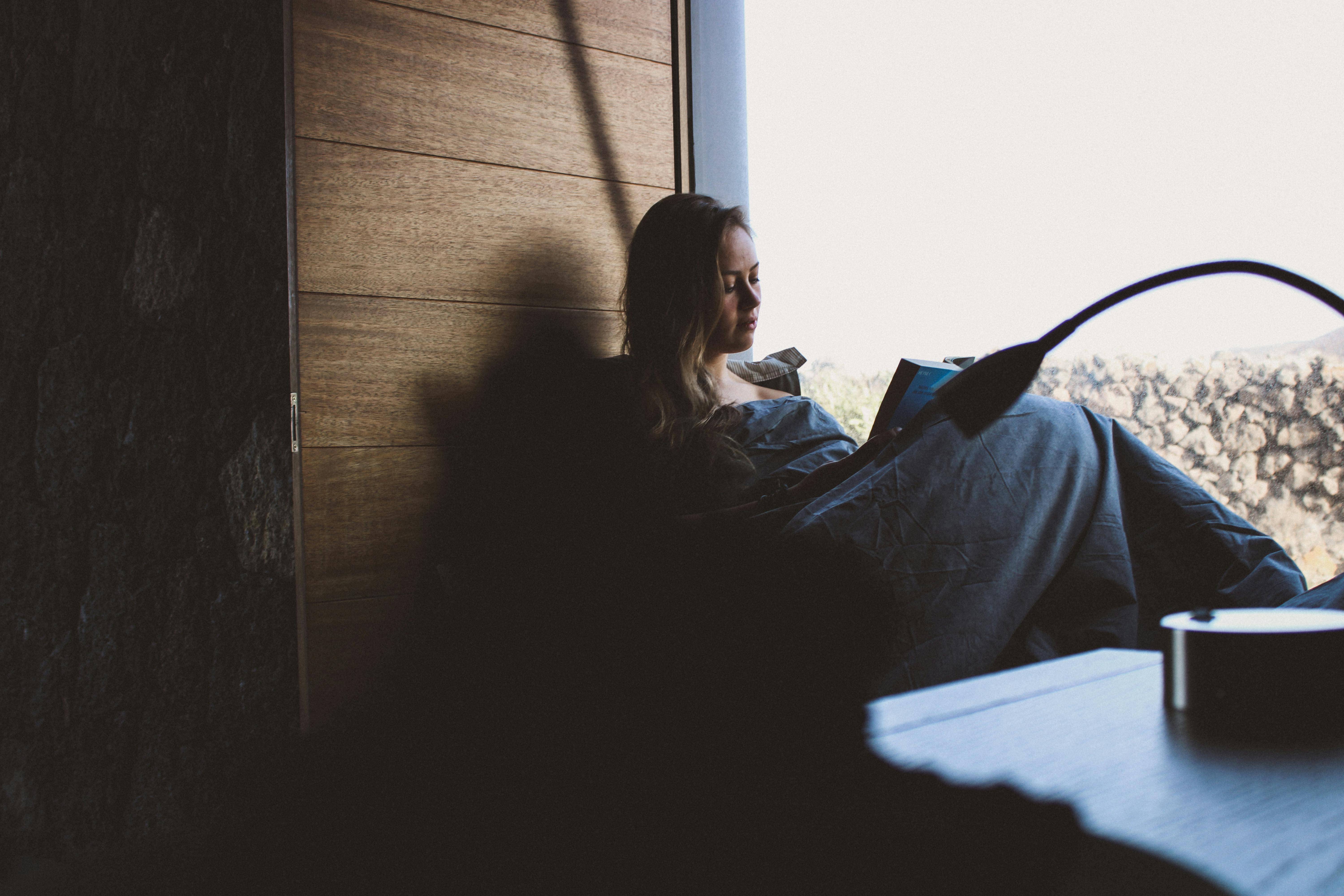 Woman reading quietly by a window in soft natural light for a self-trust and emotional healing blog article