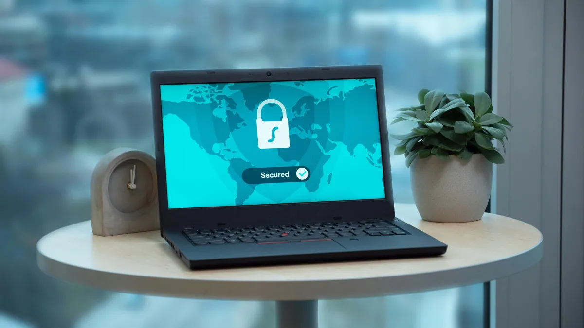 A laptop sits on a tabletop. An image of a locked padlock and word "Secured" appears on the laptop screen.