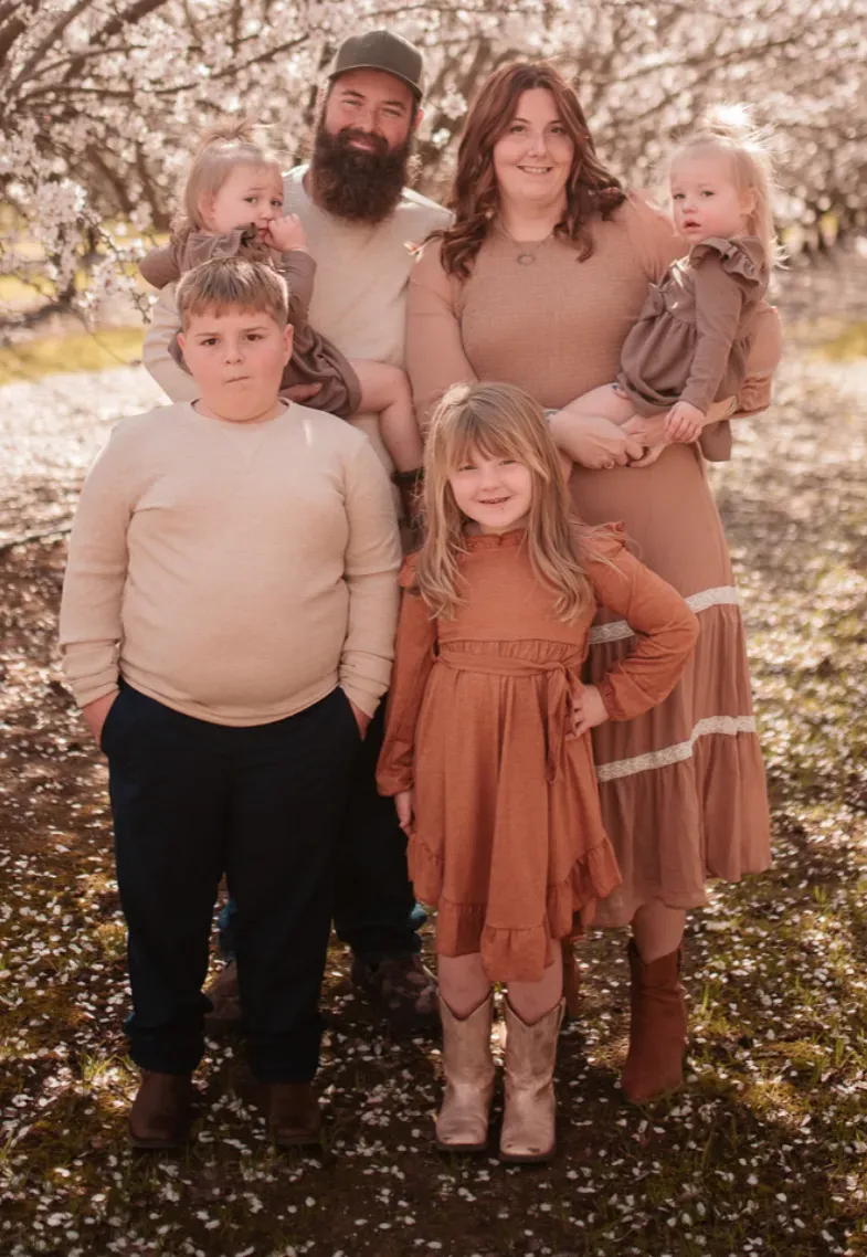 Hunts Hauling & Junk Removal LLC Family photo in a spring blossom orchard with parents and four children wearing coordinated earthy toned outfits.