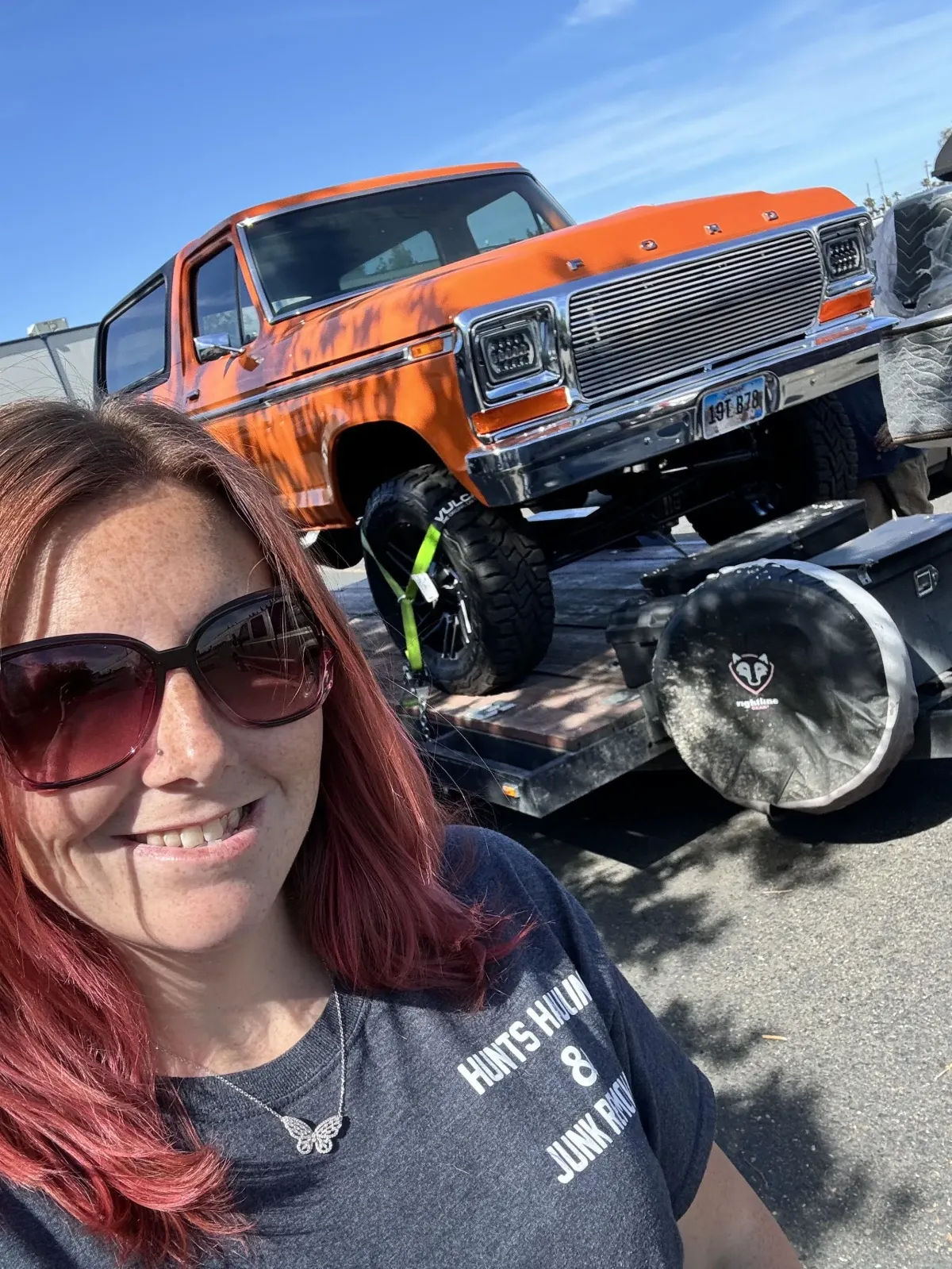 A woman smiling in front of an orange classic Ford truck on a trailer for Hunts Hauling & Junk Removal LLC services.