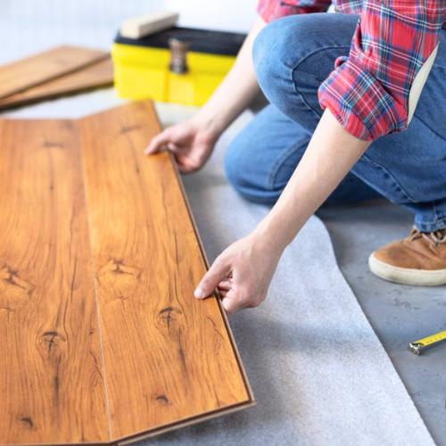 man in a plaid shirt installs plank flooring in a basement, for basement finishing contractor olathe ks