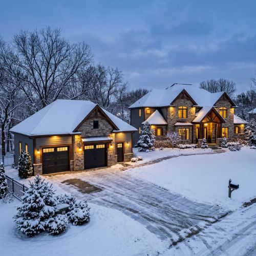 A new detached garage next to a high end house in Olathe, KS in early evening. It is winter and there is about 3 inches of snow cover.