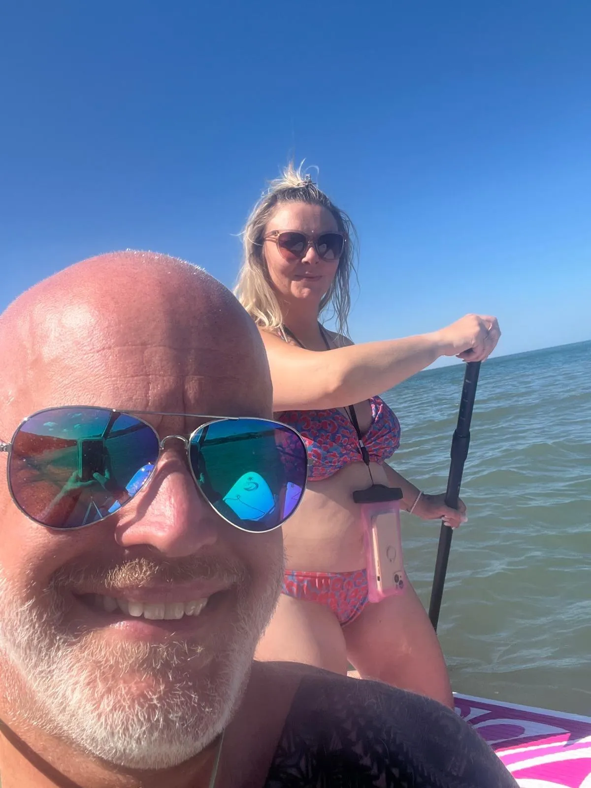 Happy couple paddleboarding together on calm water, showing a healthy relationship where a successful independent woman maintains her freedom, fun, and connection while being in love.