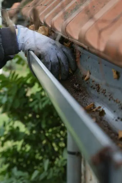 Gloved hand clearing leaves and dirt from a home gutter system during a professional clean in Auckland