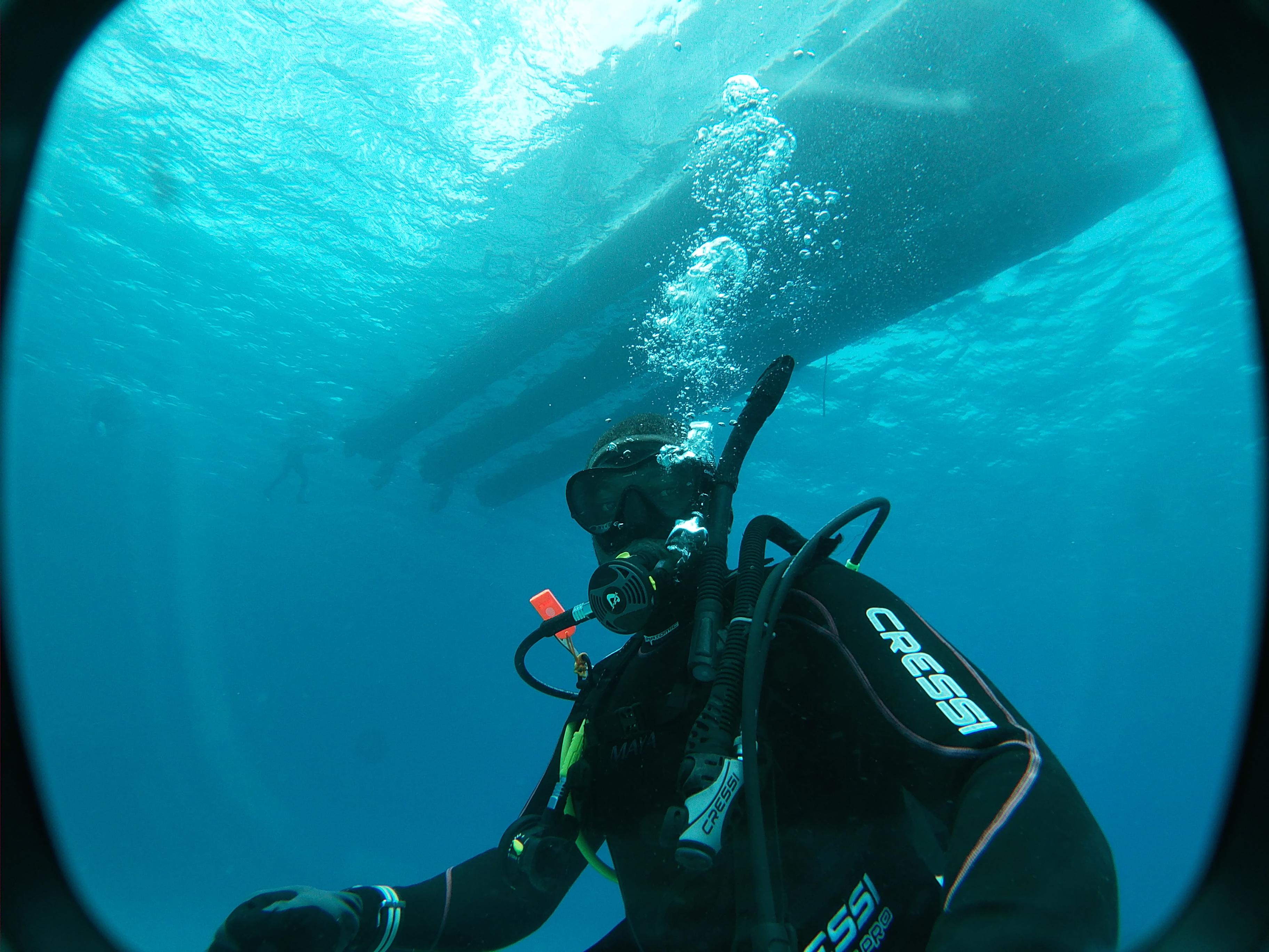 A friendly support team member, male, early 30s, sitting at a modern desk with a headset, smiling while assisting a client via laptop. The office features nautical decor, and sunlight streams through large windows, creating a welcoming, professional atmosphere.