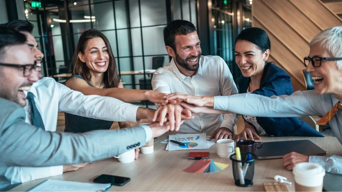 Synonym for cultivate environments of encouragement and trust: team holding hands across the table, smiling happily