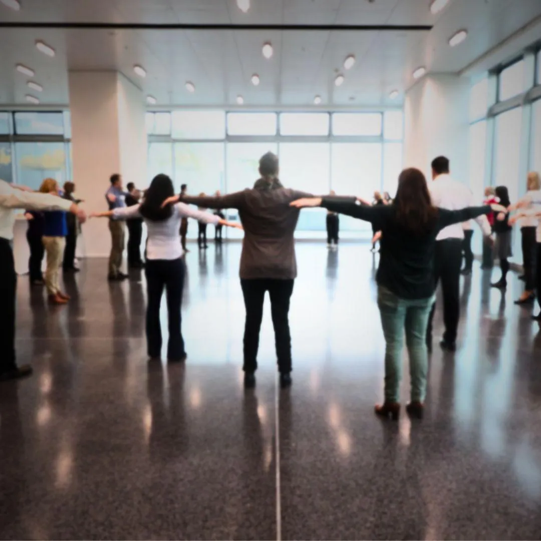 Participants of a workshop facilitated y Birgit Gosejacob standing in a wide circle with outstreched arms