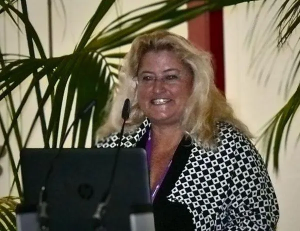 Birgit Gosejacob smiling at the lectern with tropical plants in background