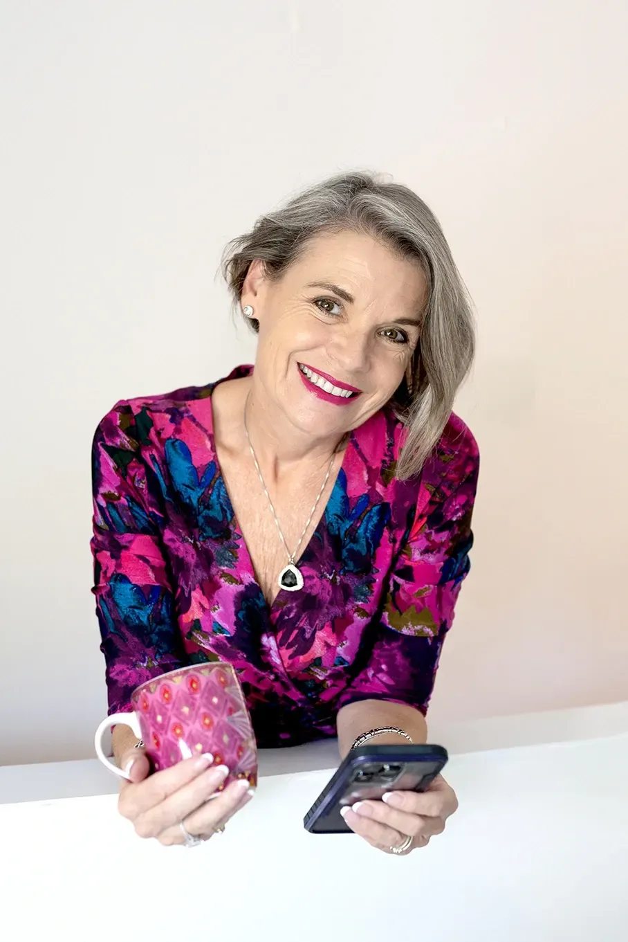 Ann Whitaker smiling while holding a phone and glass, ready for a 30-minute discovery call with a client