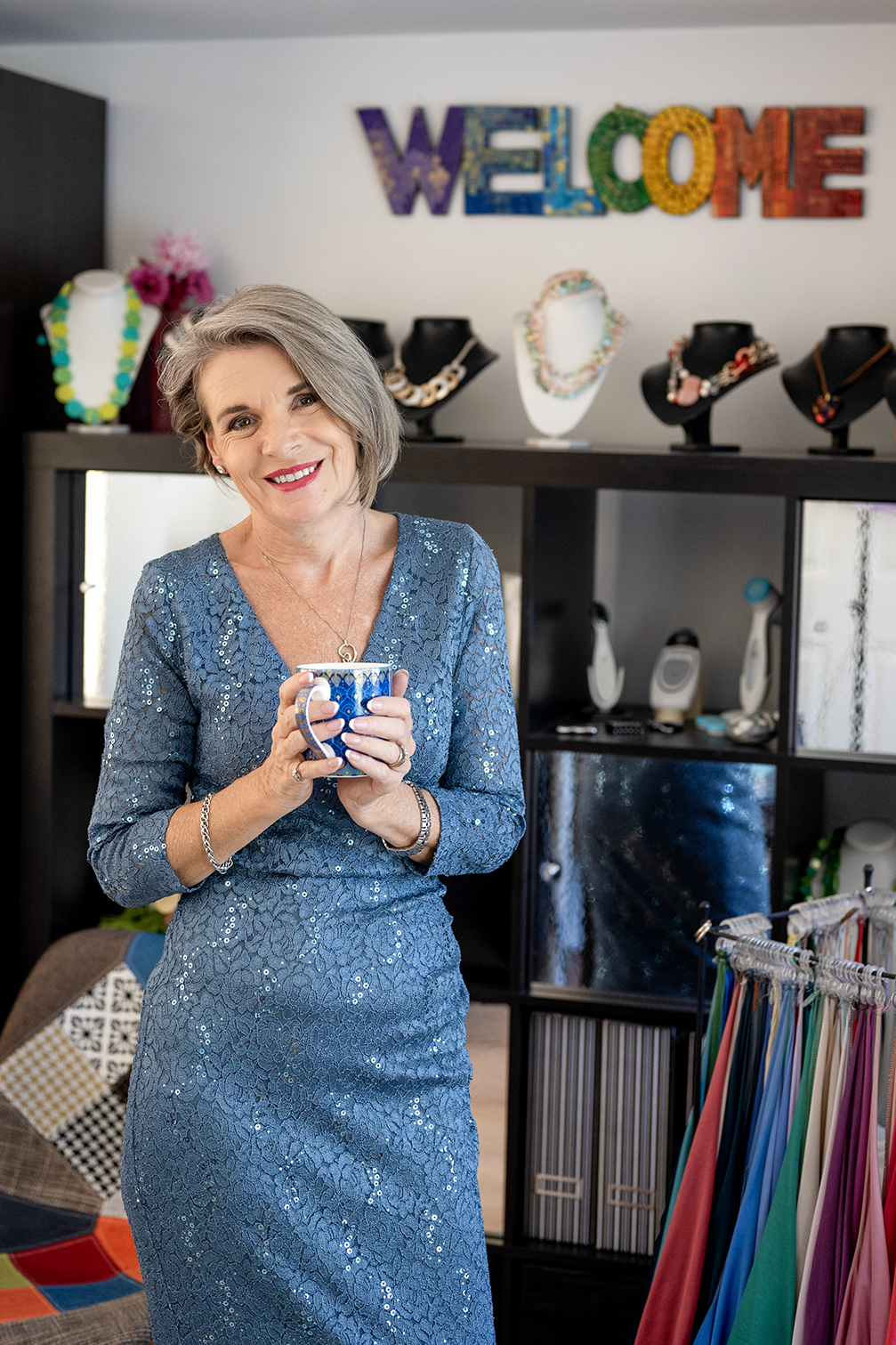A woman in her fifties wearing a sparkling blue dress holding a mug in both hands