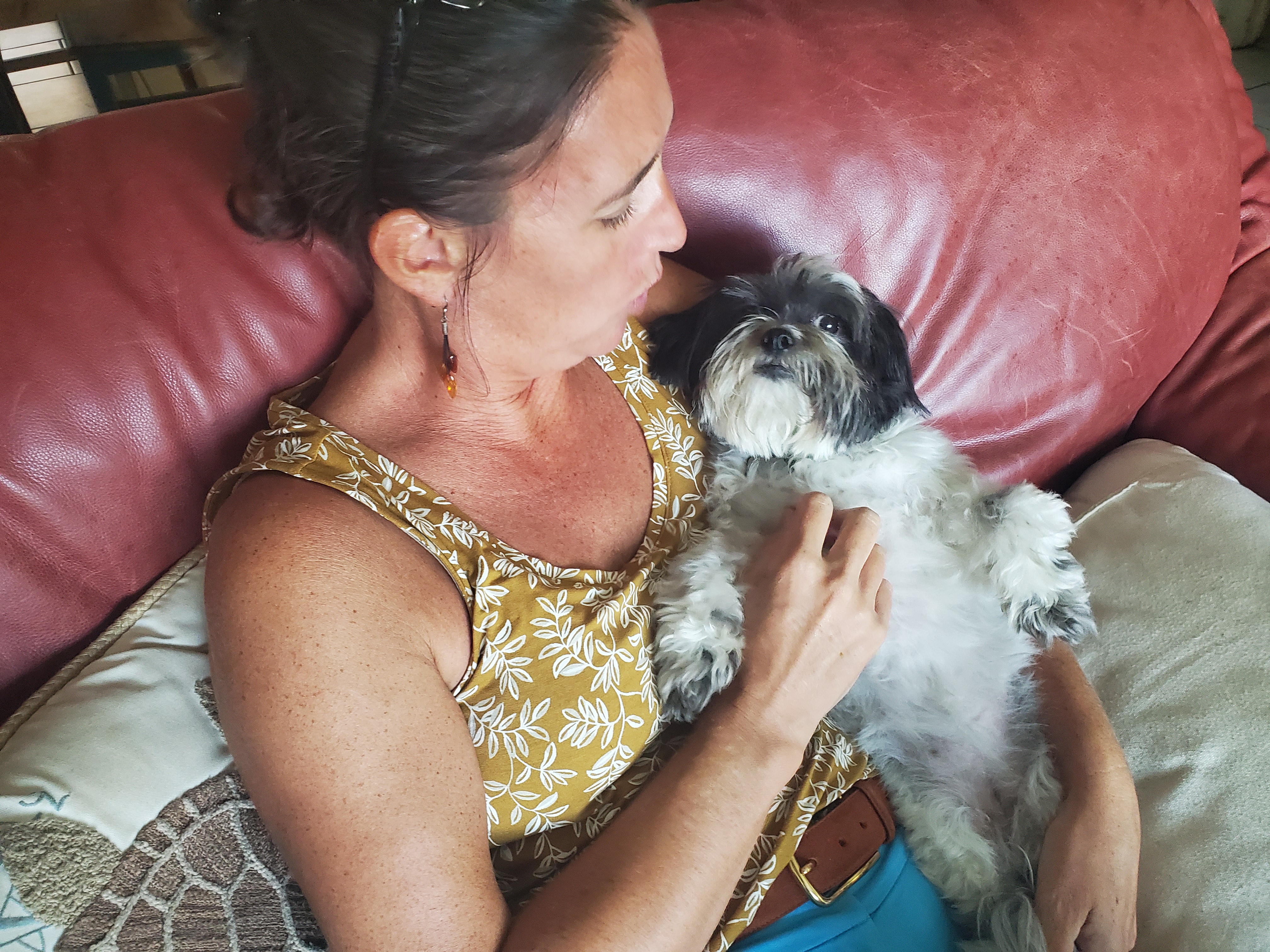 Woman cuddling a small black-and-white dog on a couch.