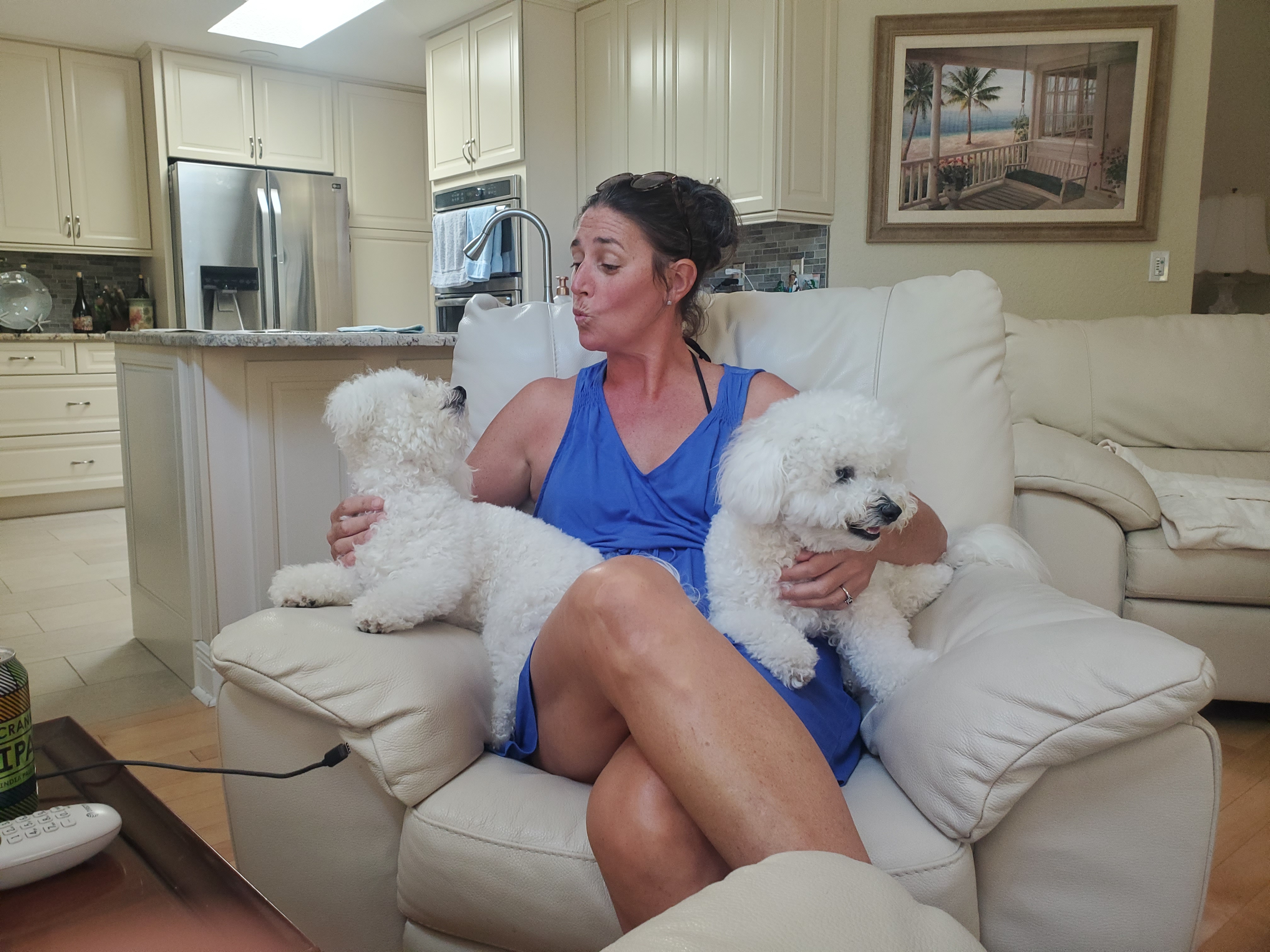 Woman relaxing on a couch with two fluffy white dogs in her lap.