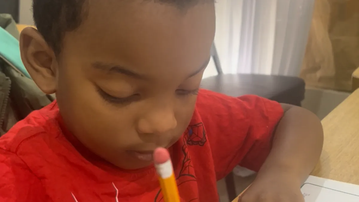 Boy holding a tambourine while watching the teacher on his tablet