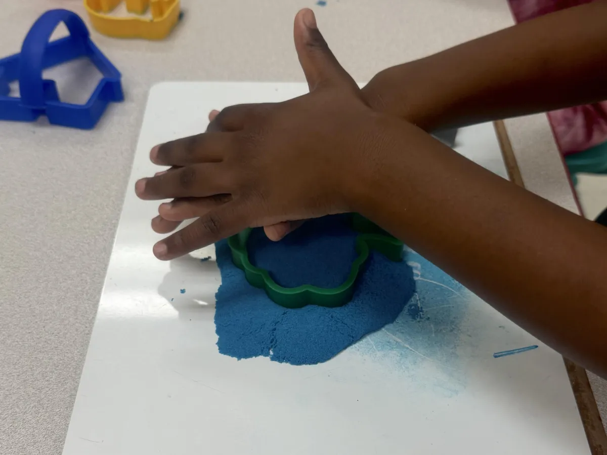 Child writes A in green sand