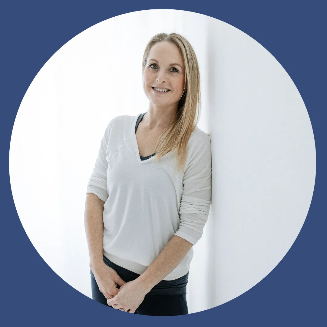 Charlotte stood against a white wall with a rolled up yoga mat