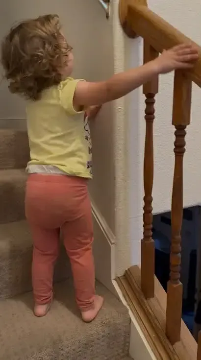 Toddler standing near staircase railing, illustrating child safety awareness, supervision needs, and changing home environments.