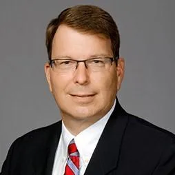 four people all on laptops, two men and two women, listen to person talking in a board meeting