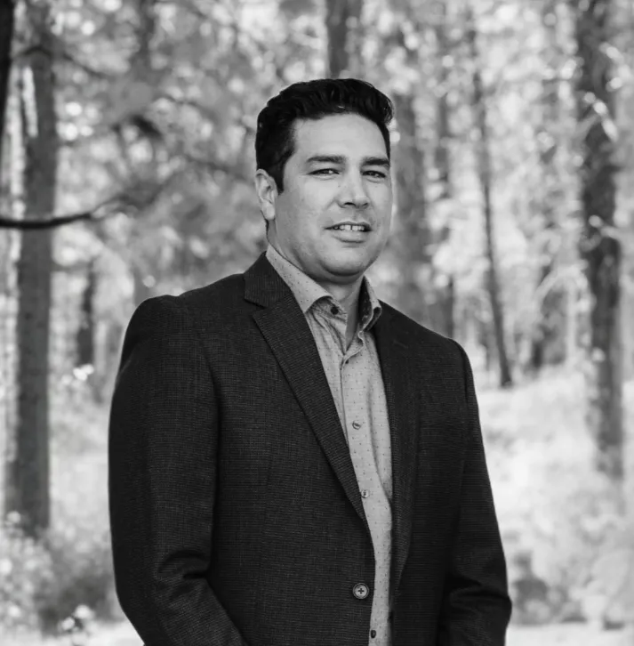 four people all on laptops, two men and two women, listen to person talking in a board meeting
