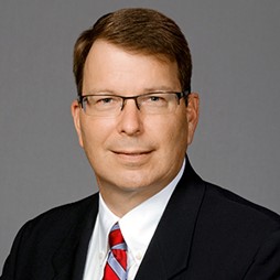 four people all on laptops, two men and two women, listen to person talking in a board meeting