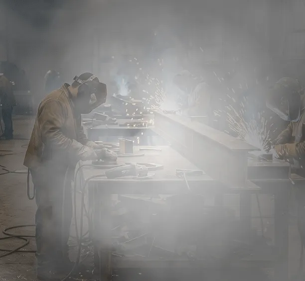 An extremely hazy weld shop with workers cutting and welding at workstations