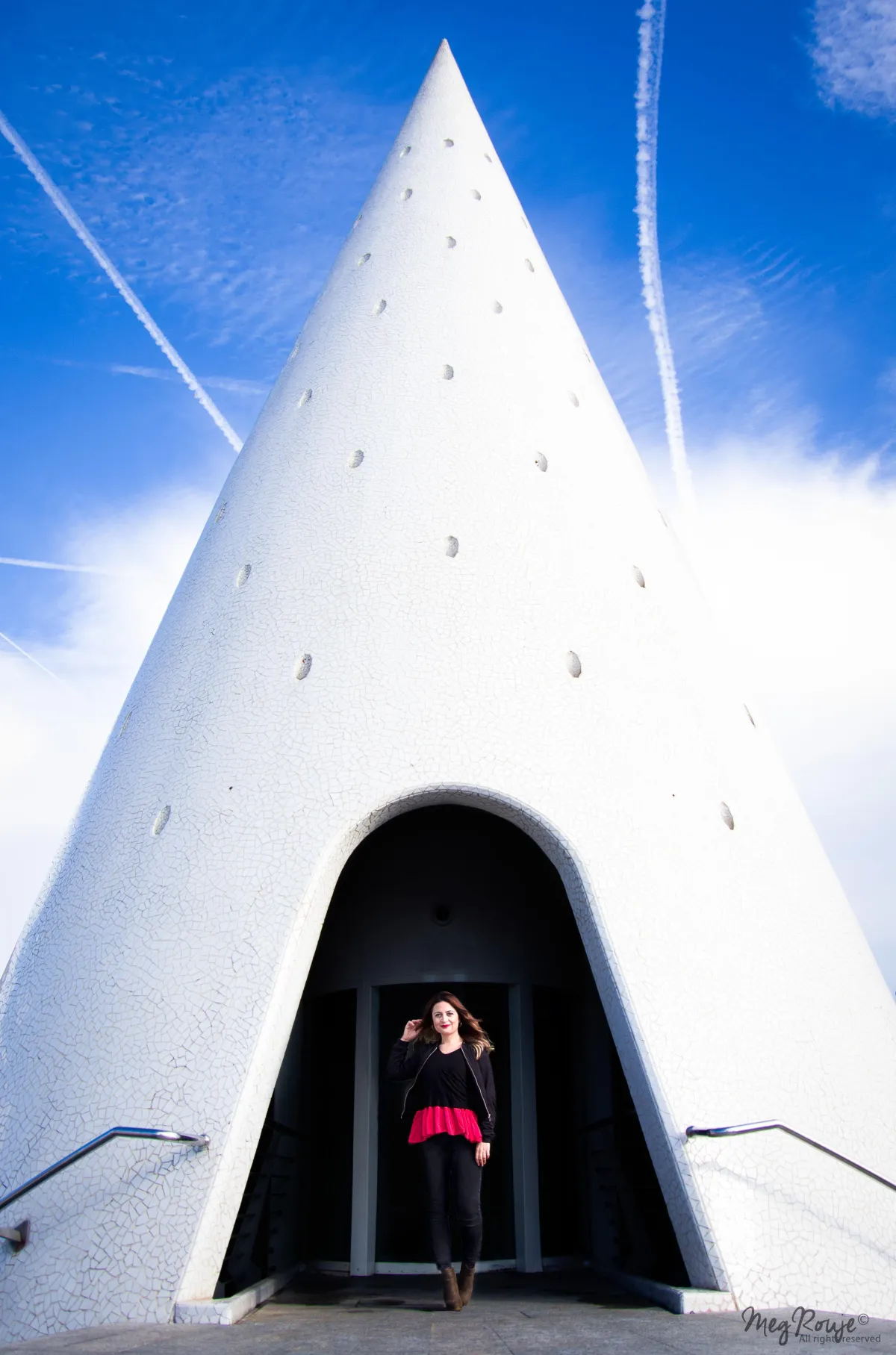 editorial photo of a woman posing at the city of arts valencia with blue sky and contrast red and black clothes